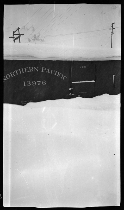 Photo of a train car in the snow. The side of the car reads "Northern Pacific 13976." The snow is piled up a few feet around the car.