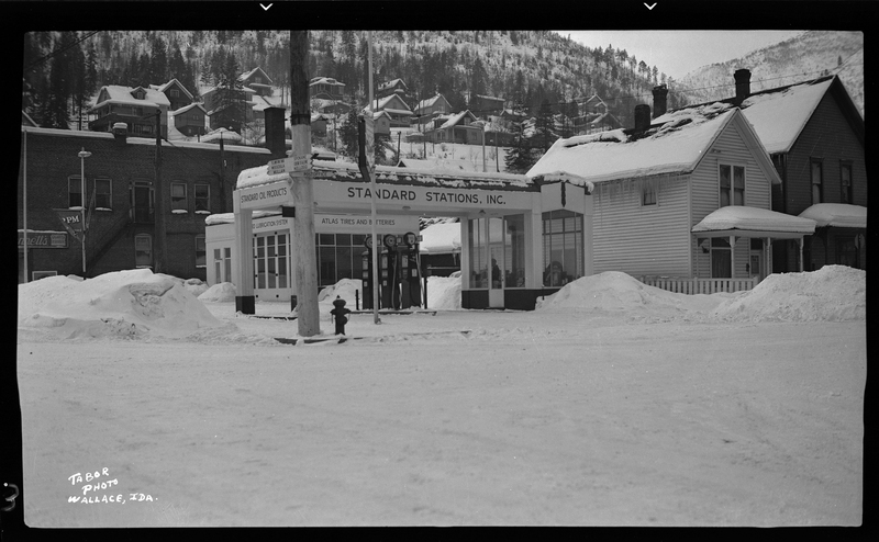Photo of the Standard Stations, Inc. building in the snow in Wallace, Idaho. It appears to be a gas station, and there are gas pumps visible under the roof. 