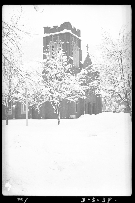 Photo of a snow covered building, possibly a church, in Wallace, Idaho. Snow covered trees surround the building, and the ground around it is also covered in snow.