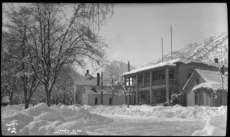 Photo of a few snow covered houses and trees, labeled "Storm King." The road in front of the houses had been previously plowed, leading to piles of snow on the sides.