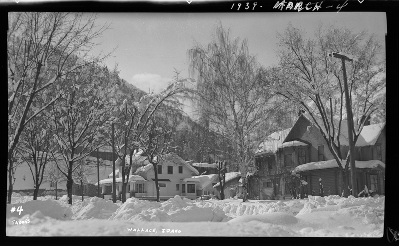 Several snow covered houses and trees are visible, as are piles of snow on the ground, in Wallace, Idaho. The piles appear to be from shoveling or plowing.