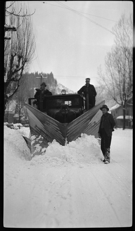 Photo of three men standing on or next to a snow plow. Two of the men stand on the sides of the plow and the third stands in front of it. They are all looking at the camera.