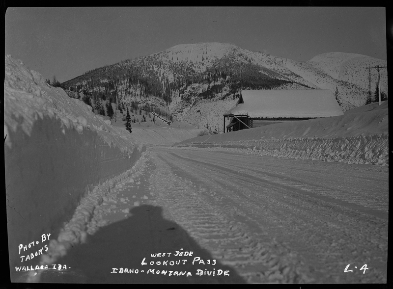 Photo of the west side of Lookout Pass on the Idaho-Montana Divide. The snowy road had previously been plowed, and there is a building covered in heavy snow off to the side.