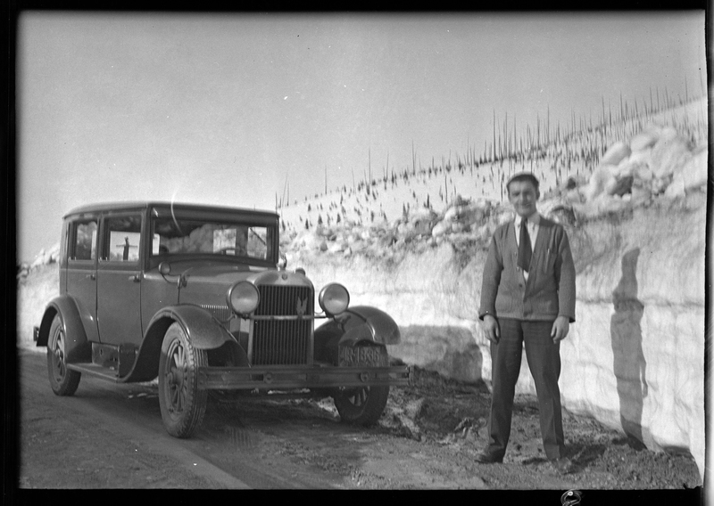 An unidentified man stands in front of a parked car at Lookout Pass. There is a wall of snow behind him.
