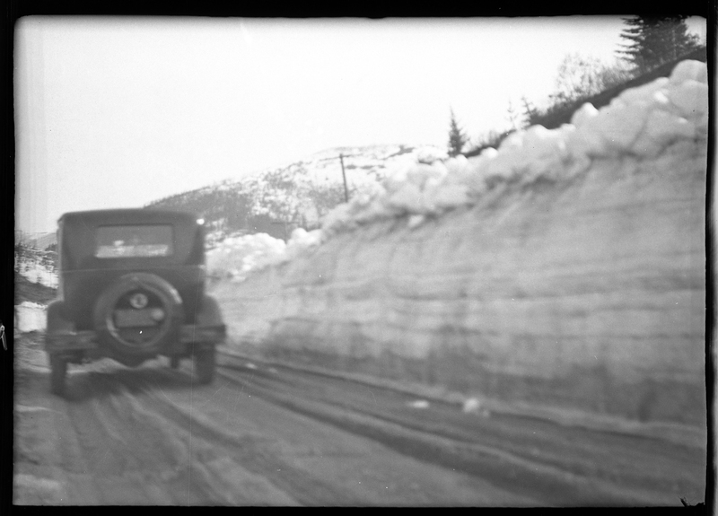 Photo of a car parked on the side of the road at Lookout Pass. There is a tall wall of snow next to the car.
