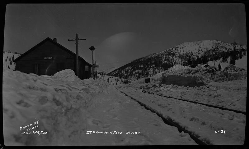 Photo of a building at Lookout Pass on the Idaho-Montana Divide. There is snow covering the ground, and what is likely railroad tracks. The ground in the distance is covered in trees and snow.