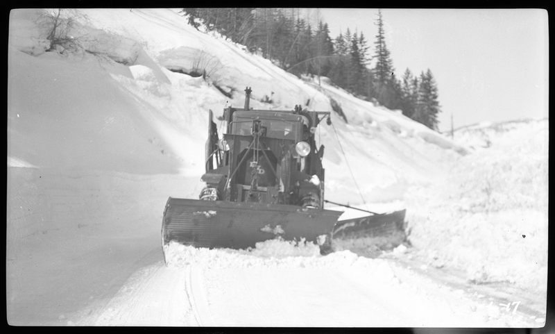 Photo of a snow plow clearing the road at Lookout Pass. The snowplow is facing the photographer. Trees can be seen in the background.