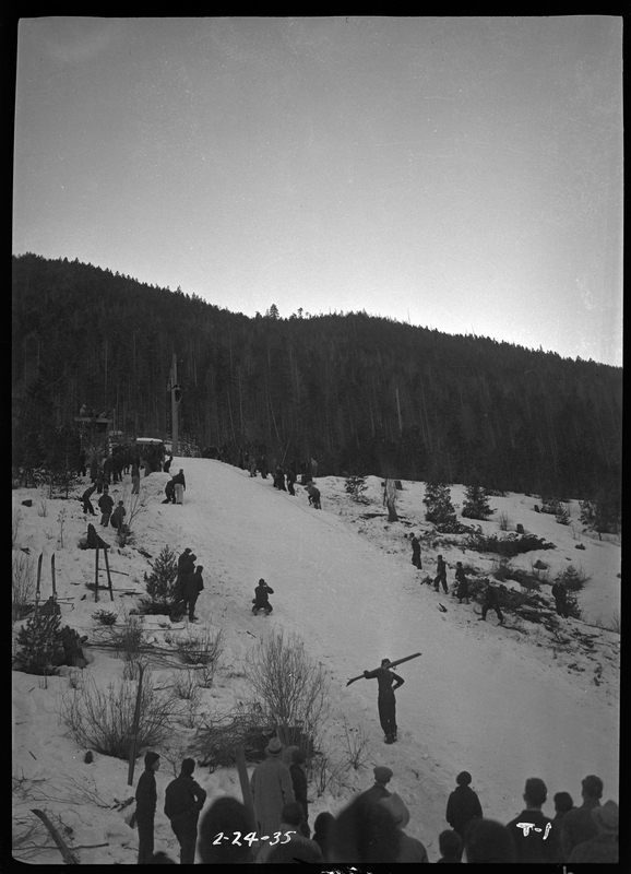 Photo of the ski jump hill located at Lookout Pass for a ski jump event. There is a ground of people at the base and a few people on the sides of the hill.