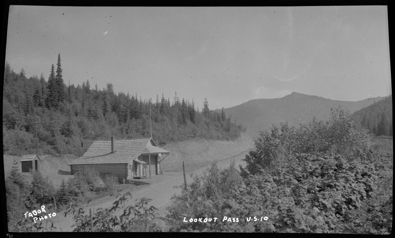 Photo of a log built building at the side of the road at Lookout Pass. The building is off a dirt road and trees surround the area.