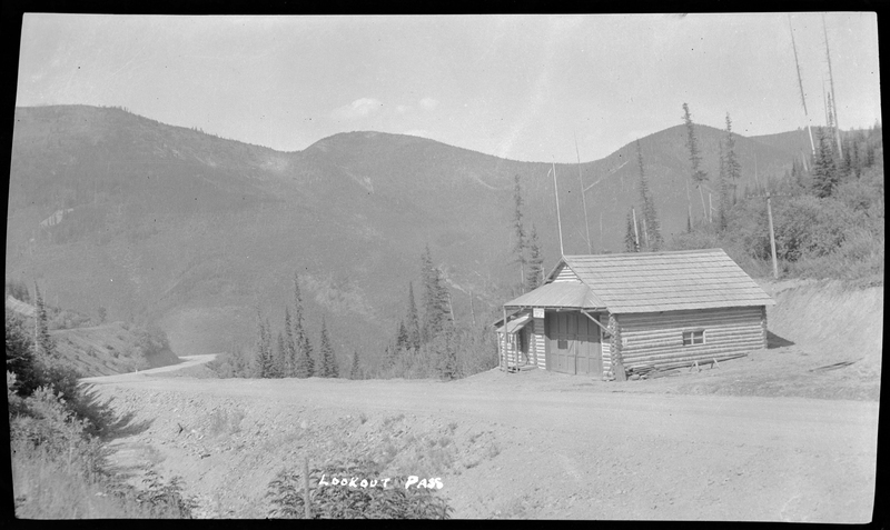 Photo of a log built building at the side of the road at Lookout Pass. The building is off a dirt road and trees surround the area.