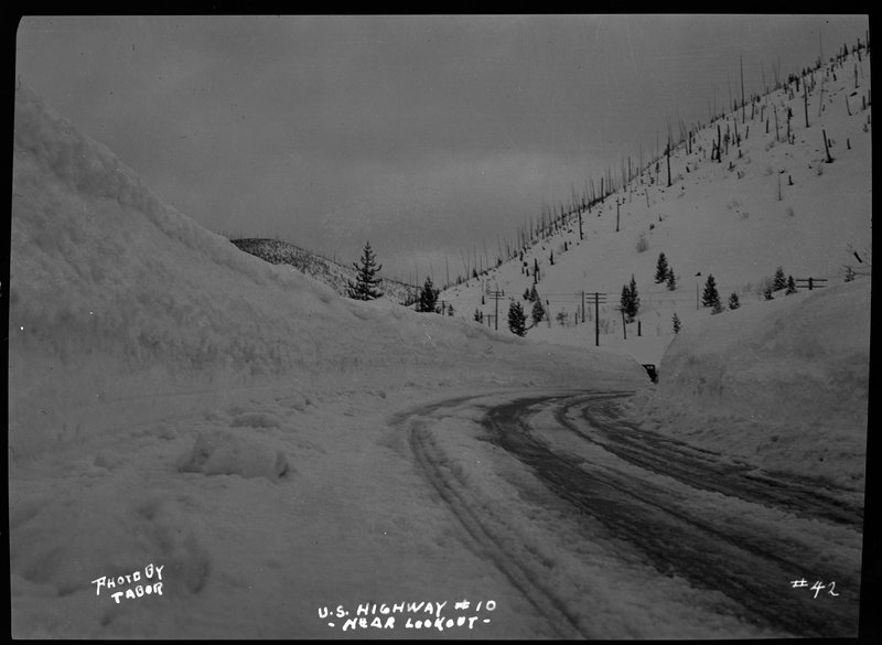 Photo of a snow covered road near Lookout Pass. There are walls of snow piled up on either side of the road, suggesting regular plowing.