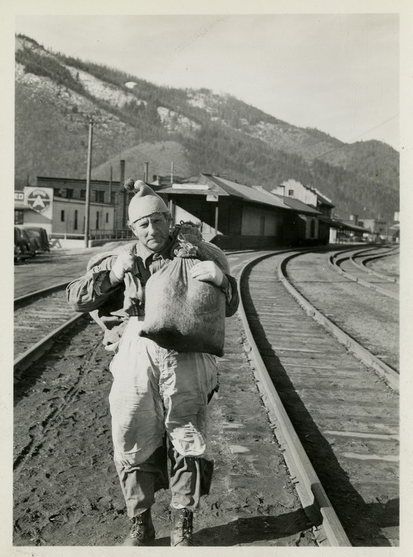 Man standing near railroad tracks and carrying bags over his shoulders near the Union Pacific depot.