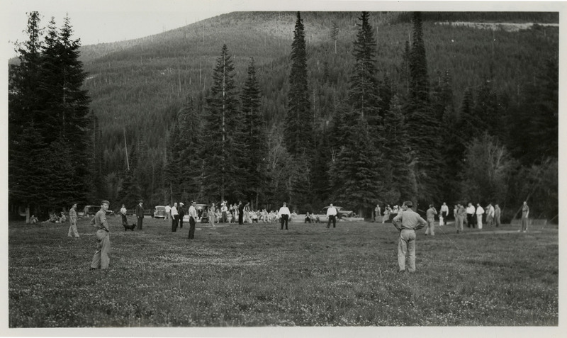 A crowd of people in uniform mill about a large field. There are no names on the back of the photo.