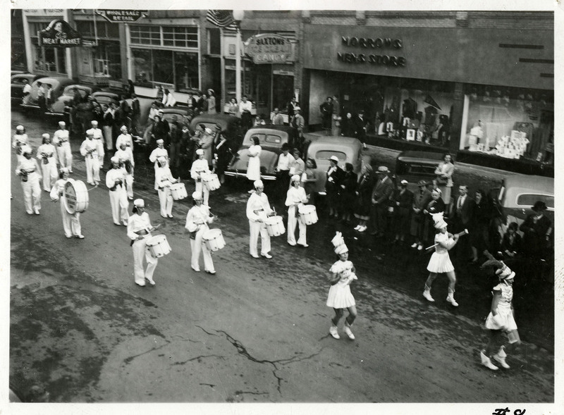 Several majorettes lead a marching band down the street.