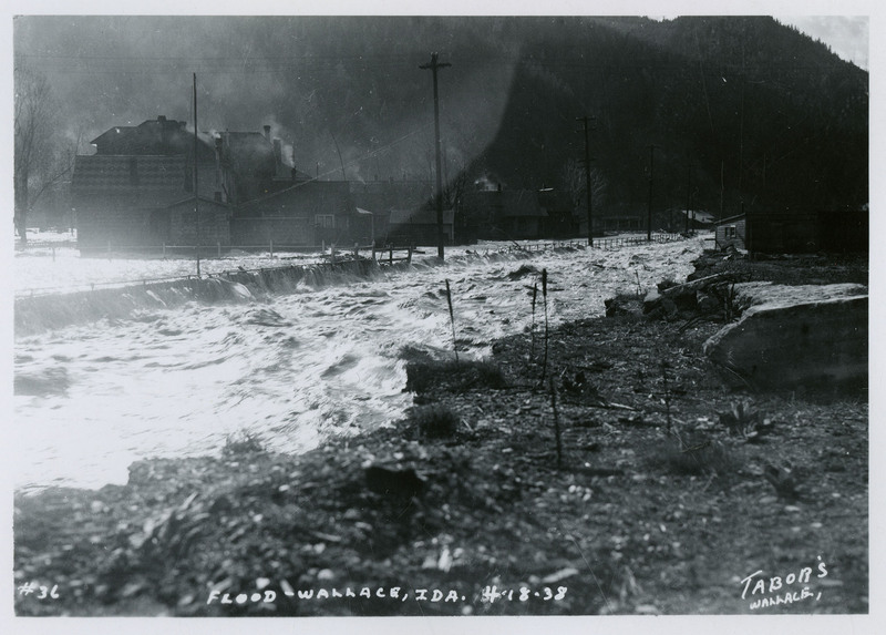 Water rushes towards previously dry land during the Wallace flood. A few buildings and telephone poles are visible in the background.
