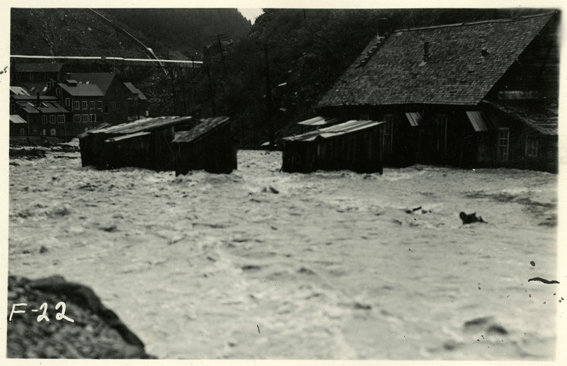 A rush of water reaches up to the bottom of first floor windows during the Wallace flood. Several buildings have been overtaken by the water. Unknown pieces of debris are floating in the water.