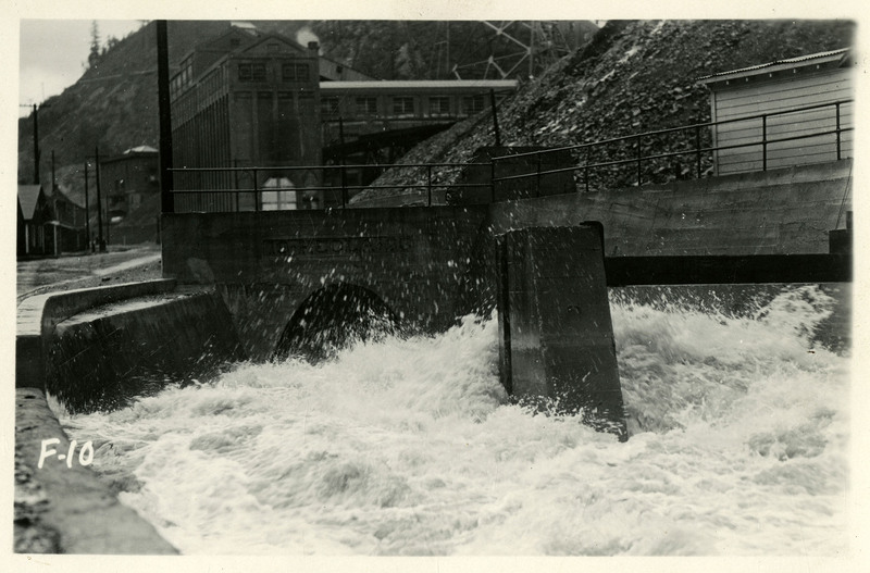 Floodwaters rush towards a tunnel during the Wallace flood. Several buildings and telephone poles are visible in the background.