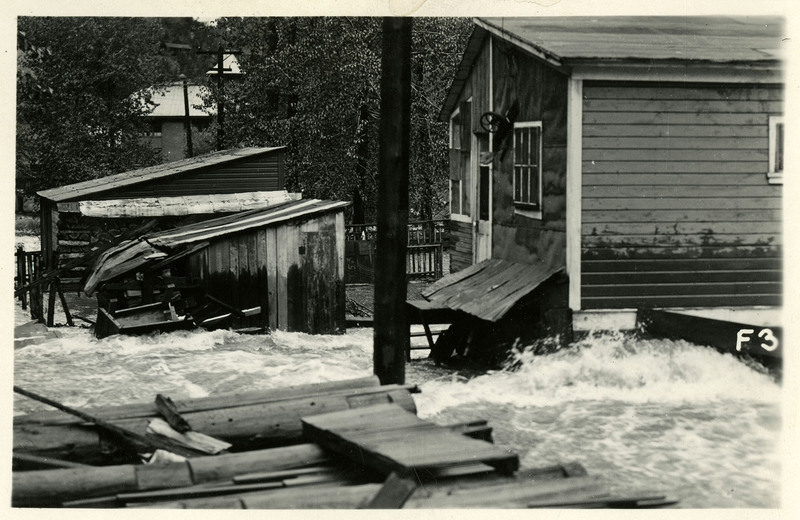 Water rushes past several buildings during the Wallace flood.