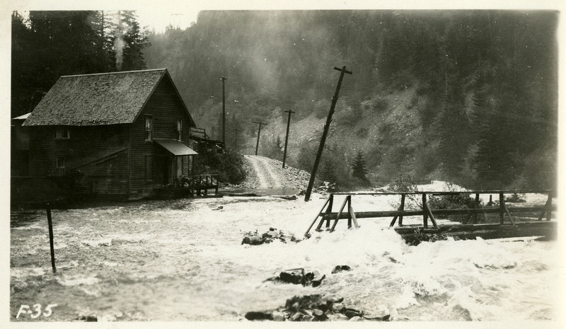 Flood waters cover a road and nearby bridge during the Wallace flood. The water is encroaching on a house and appears to have damaged a telephone pole.