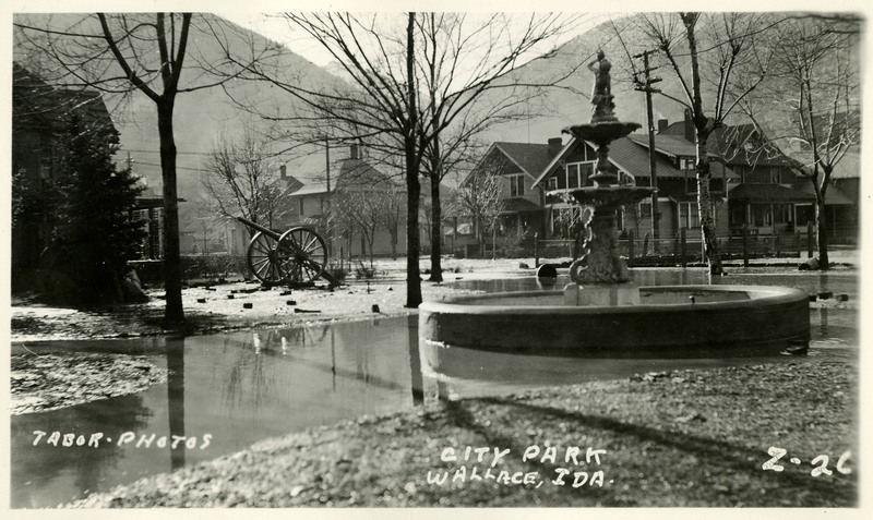 Flooding near the fountain and walkways of Wallace City Park. There are a cannon, gazebo, and variety of other buildings visible in the background.