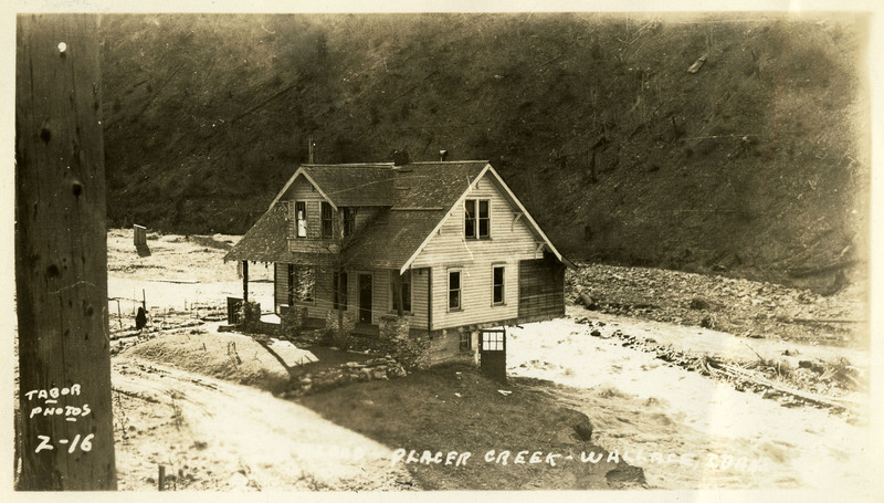 A damaged house stands at the edge of Placer Creek during the Wallace flood. Much of the ground surrounding it appears to have been swept away by the tide.
