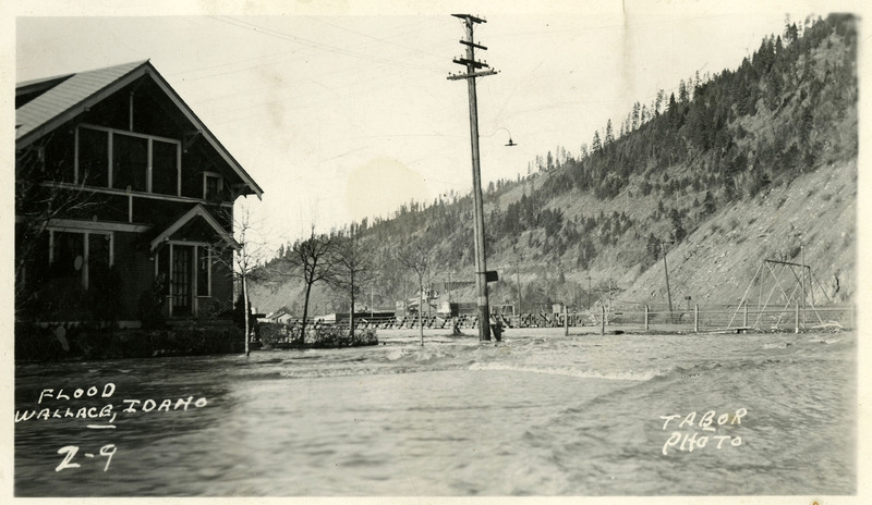 Floodwaters surround a building during the Wallace flood. A telephone pole, fence, and additional structures are visible in the background.