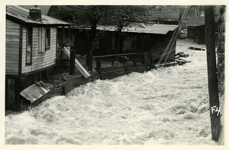 Flooding pushes up against several houses during the Burke Canyon flood. Some pieces of debris can be seen floating in the current in the background.