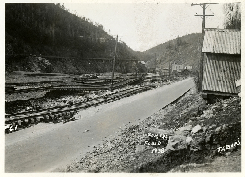 A view of the damaged railroad tracks following the Burke Canyon flood. there are several buildings and a road also visible within shot.