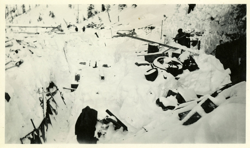 A person appears to be removing snow from a pile of debris at Jack Waite mine. Two more people are visible in the background of the photo.