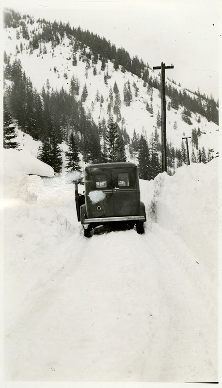 A car with its drivers side door ajar is stopped in the middle of a snow-covered road.