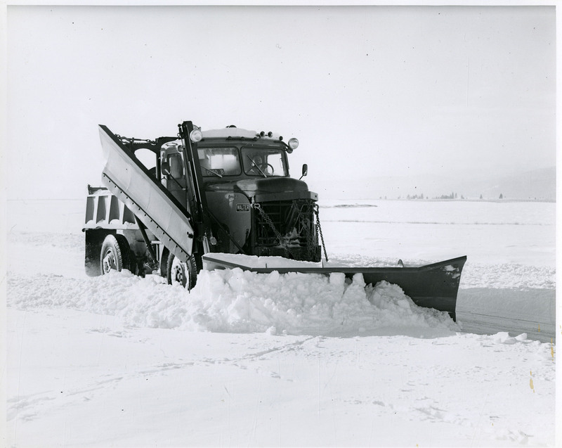A Walter snow plow clears roads near a snow-covered field.