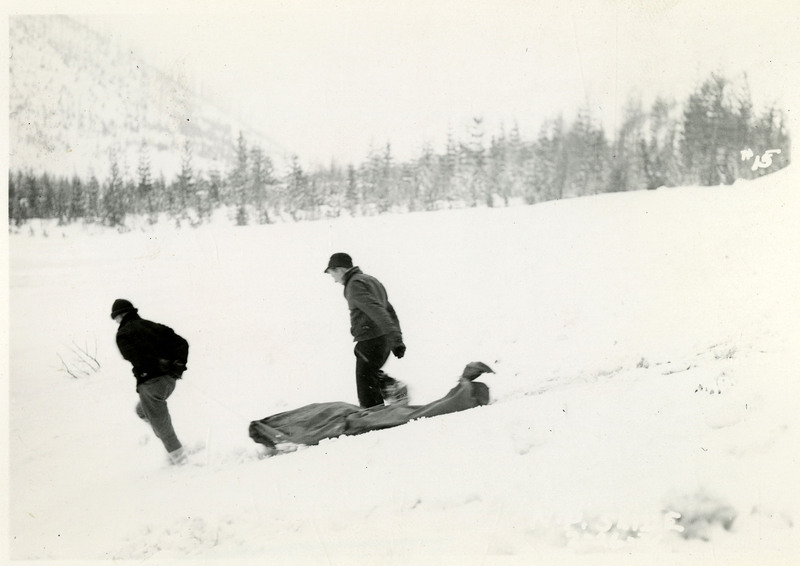 Two people drag what appears to be a body bag down a snowy hill after the Northern Pacific slide.