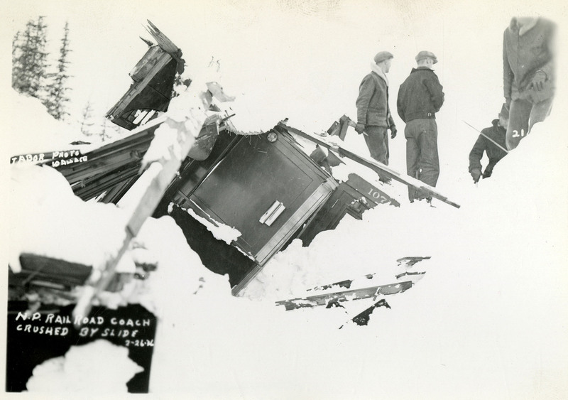 A few people stand near debris from the Northern Pacific railroad coach crushed by a slide.