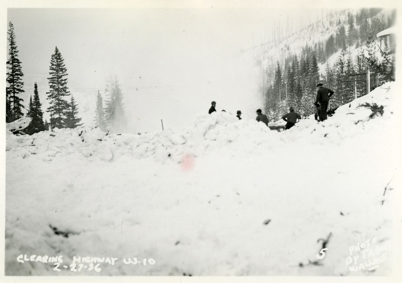 A group of people work to clear Highway US 10 after the Northern Pacific slide. Piles of snow and debris obscure the camera's view of the people.