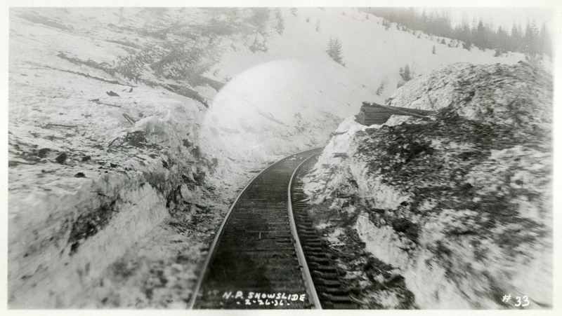 A view of the railroad after the Northern Pacific snowslide. The surrounding snow is covered in debris, but the tracks appear clear.