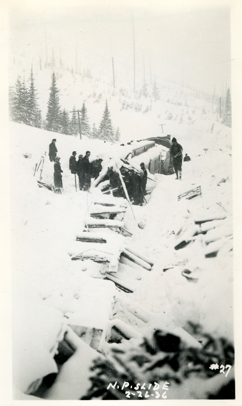 A group of people stand near Northern Pacific train damaged by snowslide and the nearby debris.