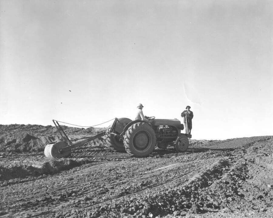 Two CCC workers from Mountain Home Camp G-99 roll out dirt area with tractor and drum. Image part of CCC-Idaho Indian Division.