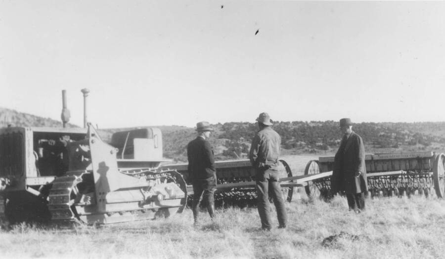 Men stand in field near drilling or reseeding machines and tractors. 'Project 138, Range revegetation, $2550. An amount of $350 was added under authority dated February 1, 1940. Project 100% complete. About 2565 acres reseeded consuming approximately 567 mandays. Soil Conservation Service furnished supervision, seed, and drills. CCC-ID furnished tractors, gasoline and oil, men and transportation.' Note: This image is part of a report by V.W. Balderson to Director of Indian Affairs, D.E. Murphy on CCC-Indian Division Projects completed by the Fort Hall Agency, Fort Hall, Idaho.
