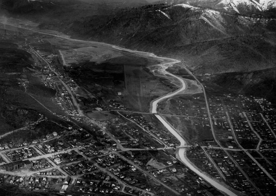 Wide aerial image of Kellogg, Idaho and the Coeur d'Alene River. The snow-capped Bitterroot Mountains are in the background.