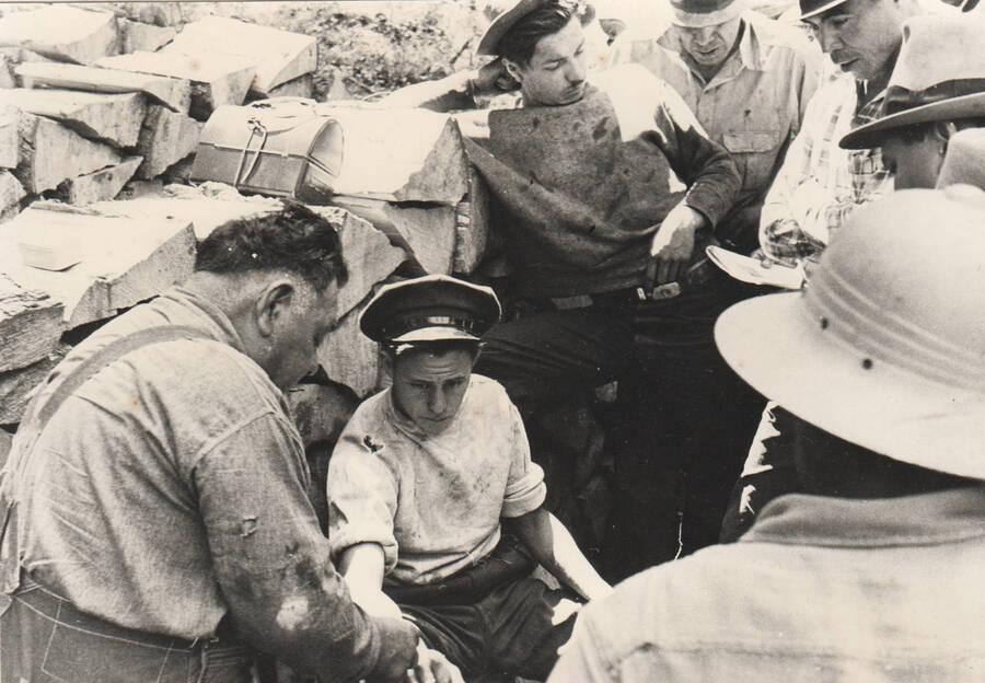 Photo text: 'First aid instruction in the field. Instruction being given in 'What to do In Case of Snake Bite'. There are rattlesnakes in the part of Idaho so special attention is given to this fact during the summer months. Leader Ed Raboin, who holds a First Aid Instructor's certificate is demonstrating with Enrollee James Taylor as the subject. A standard snake bite kit is furnished all crews during the summer months.' Note: This image is part of a narrative pictoral report to accompany quarterly enrollee program report.