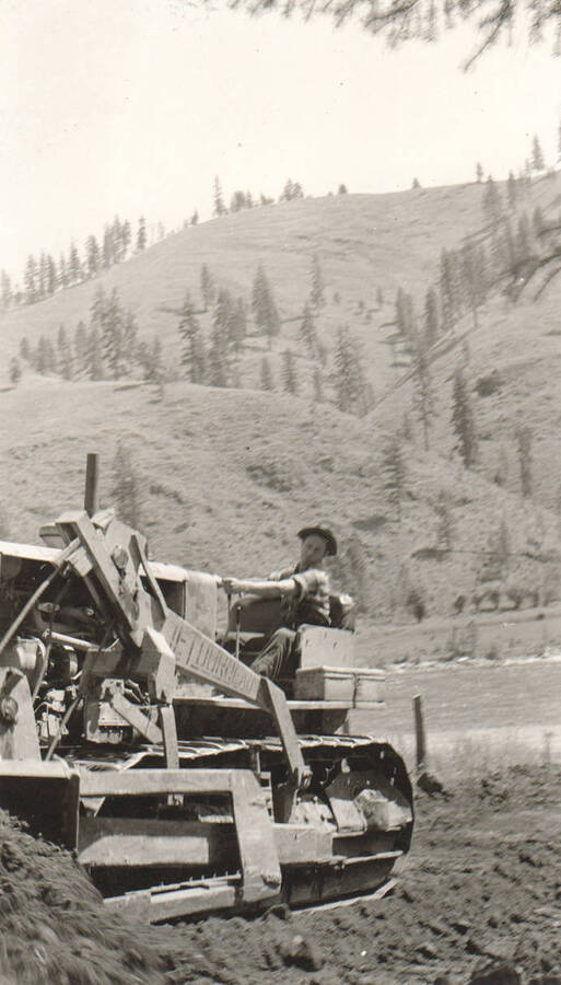 Photo text: 'Leader James Taylor bulldozing truck trail just off highway, shown just back of tracks on tractor. Beyond highway is Clearwater River.' Note: This image is part of a pictorial supplement to a report on the North Idaho Agency and the Civilian Conservation Corps - Indian Division by Sidney L. Johnston, Assoc. Forest Engineer.
