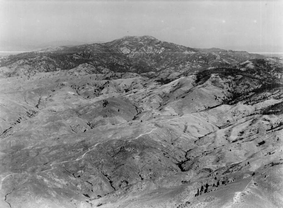 Photo text: 'Shaw's Mountain , northeast of Boise, Idaho - Showing the winding road over which thousands of miners, in the 60's poured into the Boise Basin, where at Idaho City, Placerville, Centerville, Pioneersville, and Quartzburg, between 3 and 4 million dollars in gold dust were extracted.' This image is part of a series of aerials taken by the Army Air Corps.
