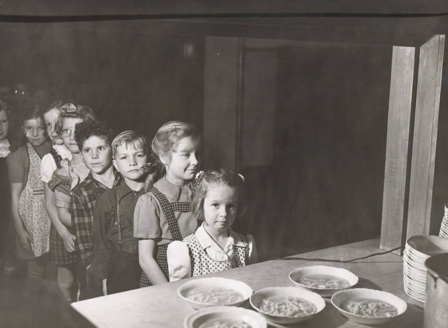 Photo text: 'Idaho WPA school lunch at Cole school, near Boise, Idaho. Two hundred fourteen similar projects were operated by WPA Idaho, during 1941-1942 school term.' Children stand in line for lunch soup. Note: This image is part of a Work Progress Administration publicity series.