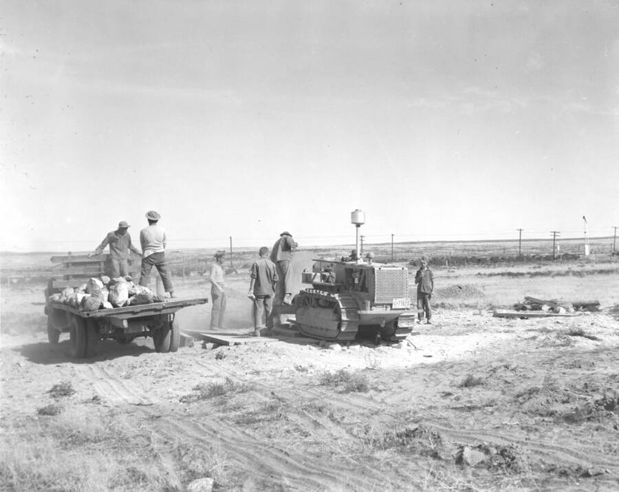 A group of CCC workers from Mountain Home Camp G-99 remove large rocks with small bull dozer and flat bed truck. Image part of CCC-Idaho Indian Division.