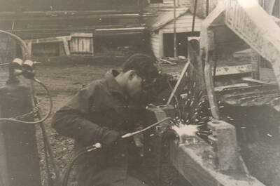 Photo text: 'Enrollee Oliver Henry wrestling the bulldozer frame.' Note: This image is part of a narrative pictoral report to accompany quarterly enrollee program report.