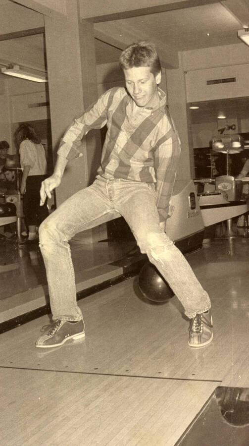 Student bowling, rolling the ball between his legs.