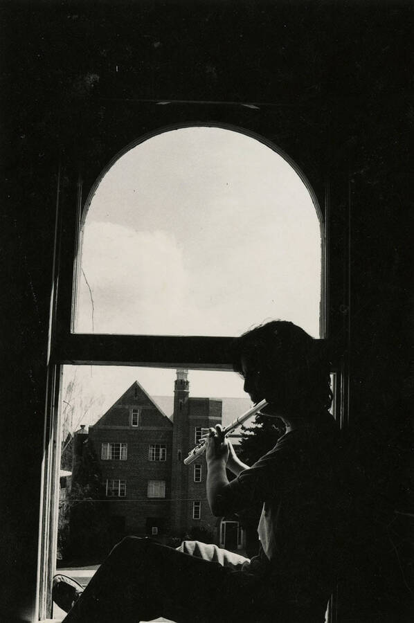A student playing flute by a window in Ridenbaugh Hall.