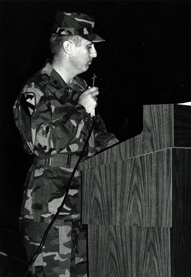 A soldier (nametape reads: ""Havre"") speaking into a microphone at a podium.