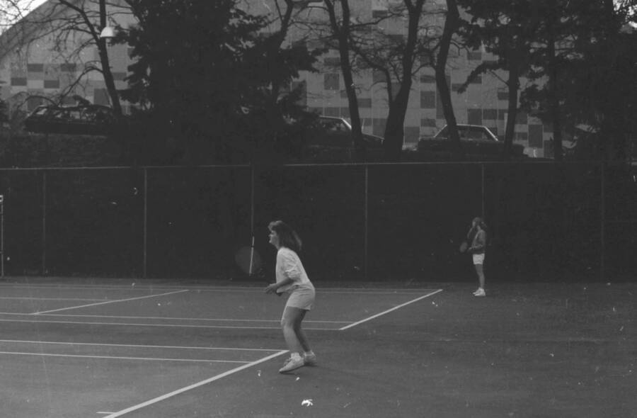 Two students playing tennis on the courts just outside of the Physical Education Building.
