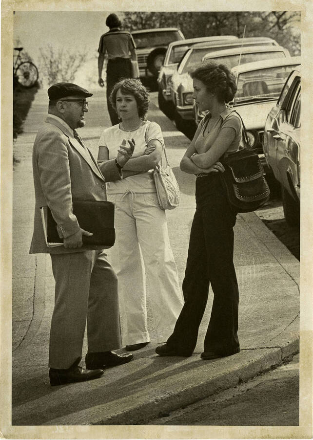Professor H. Caldwell with students on the sidewalk next to cars.